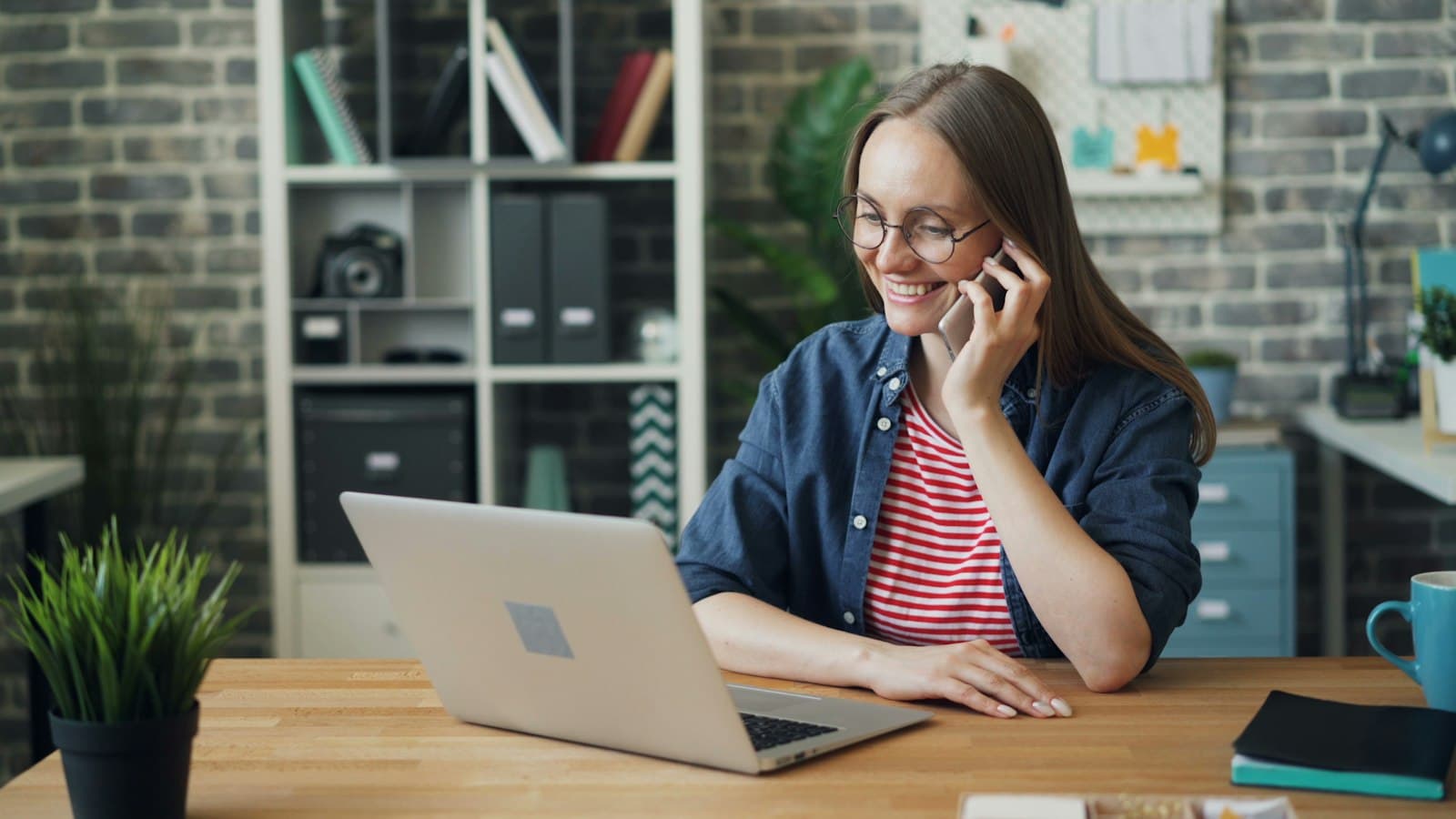 A woman on a phone call, smiling at her laptop